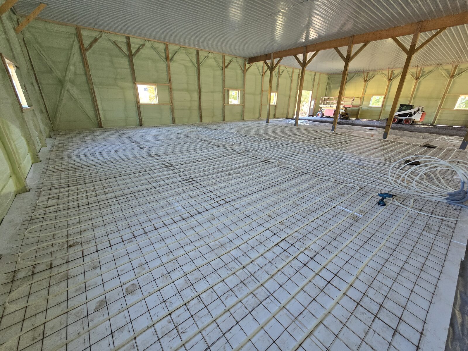 Long, evenly spaced PEX loops tied to wire mesh over foam board in a pole barn